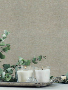 Two white candles in glass holders sit on a silver tray with eucalyptus branches and a crystal ornament, set against walls adorned with Chesapeake Tansy Distressed Wallpaper by York Wallcoverings.