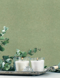 Two white candles in glass holders rest on a silver tray with eucalyptus branches and a faceted clear crystal, set against Chesapeake Tansy Distressed Wallpaper from York Wallcoverings.