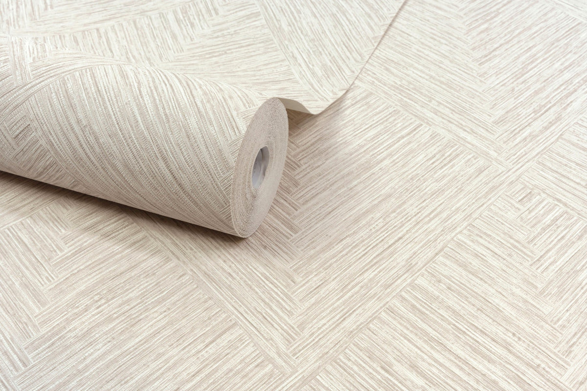 A roll of Chesapeake Hollis Textured Diamond Wallpaper by York Wallcoverings in beige, featuring a herringbone-inspired diamond pattern with textured diagonal lines for a woven appearance, is partially unrolled on a flat surface.