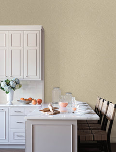 A modern kitchen featuring Chesapeake Hollis Textured Diamond Wallpaper by York Wallcoverings, complemented by white cabinets, a marble island, wooden chairs, flowers, oranges, glassware, and breakfast items like croissants and juice set on the counter.
