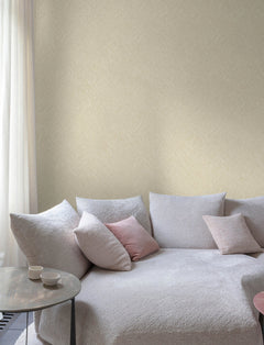 A cozy light gray sofa with pink and gray cushions sits by a round table with two cups, near a sheer curtained window and a wall adorned with Chesapeake Hollis Textured Diamond Wallpaper by York Wallcoverings.