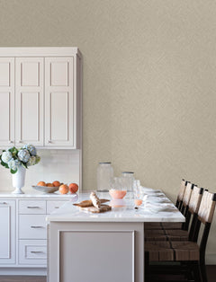 A bright kitchen with white cabinets, a marble island, four wicker chairs, glass jars, a vase of hydrangeas, oranges in a bowl, and breakfast items including croissants and juice on the counter. The walls are adorned with Chesapeake Hollis Textured Diamond Wallpaper by York Wallcoverings.