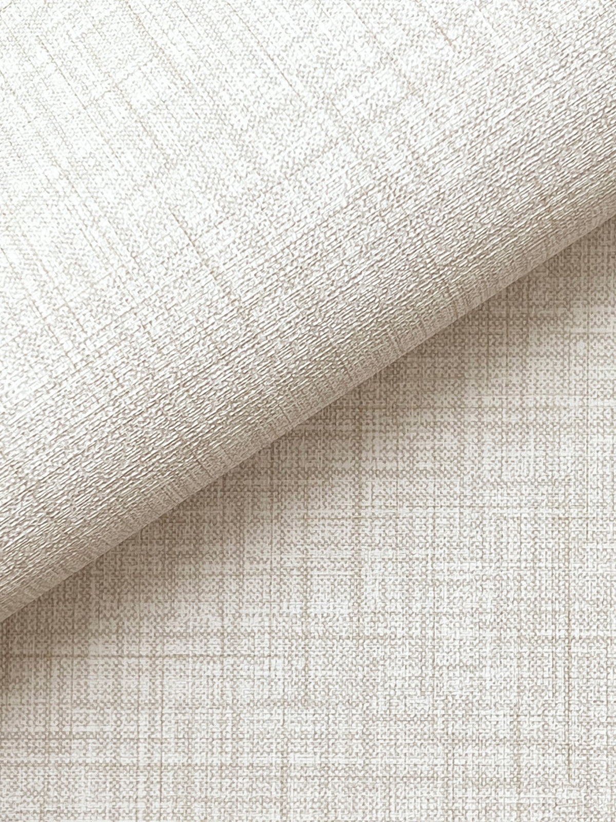 A close-up of Beau Faux Fabric Wallpaper by York Wallcoverings in light beige, featuring a subtle crisscross pattern and woven texture, with one piece rolled over another to showcase its detailed surface.