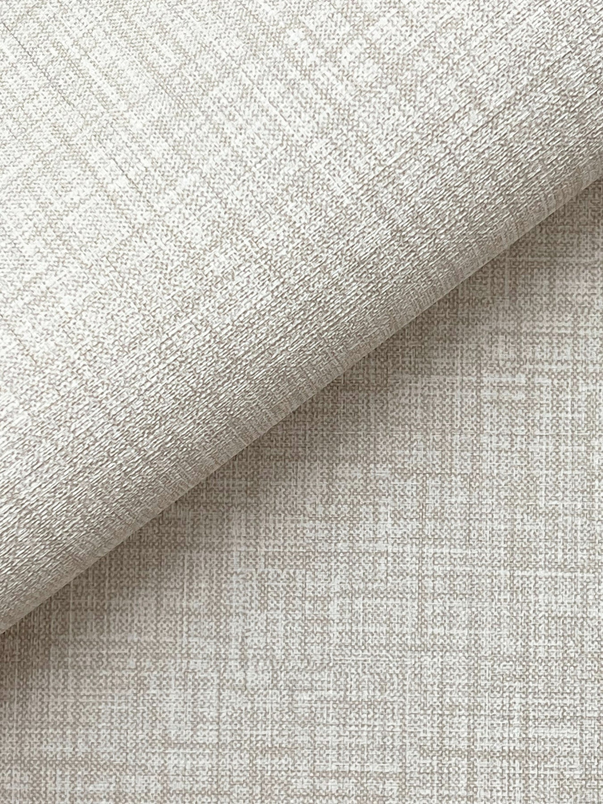 A close-up of York Wallcoverings’ Beau Faux Fabric Wallpaper, shown in beige with a subtle grid-like texture, partially folded over itself and casting a soft shadow across the lower half of the image.