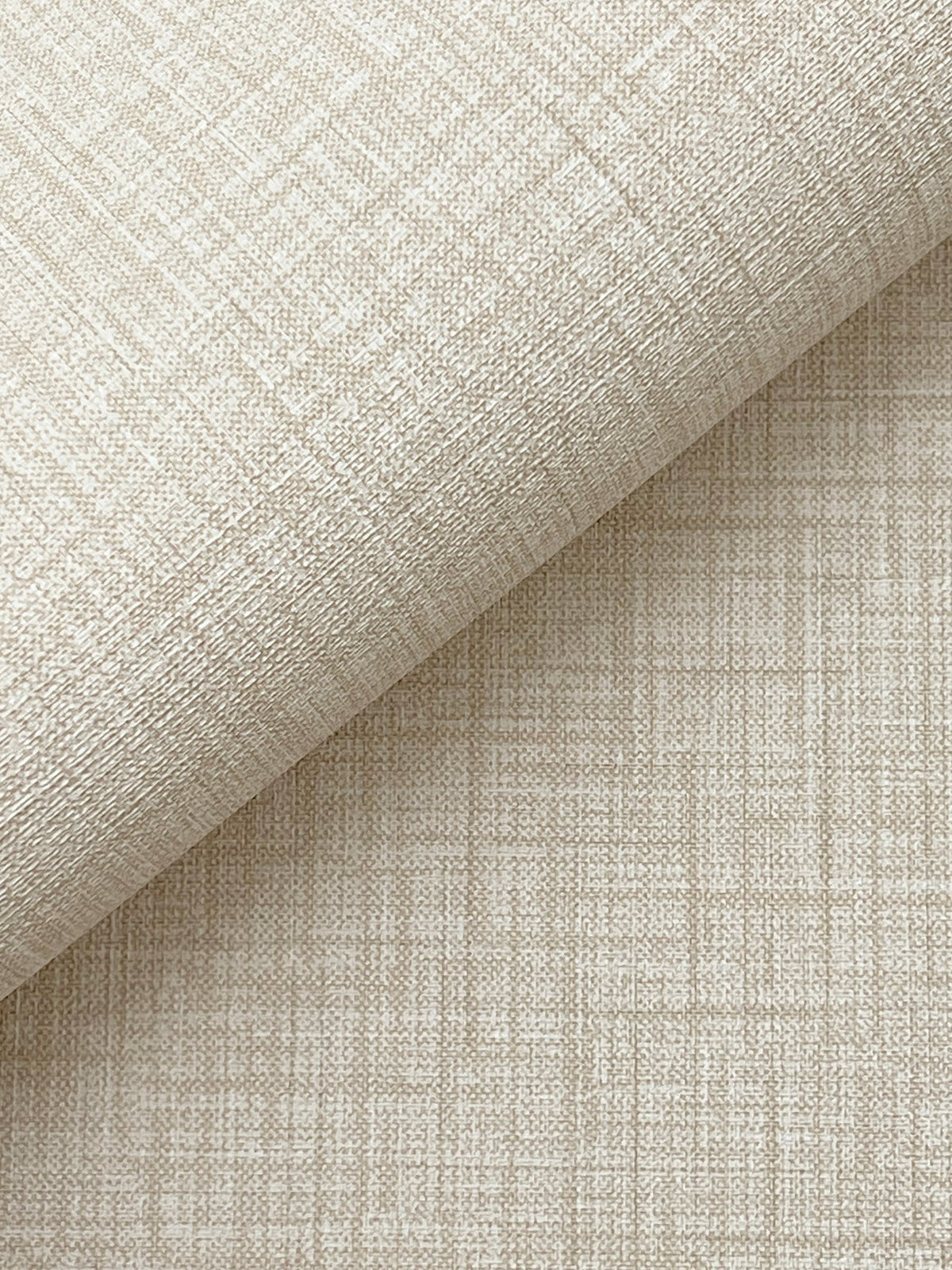 A close-up of Beau Faux Fabric Wallpaper by York Wallcoverings, featuring textured beige material with a subtle grid and crosshatch pattern, partially rolled atop a flat surface covered in the same wallpaper.