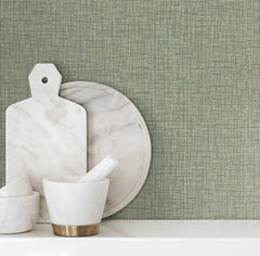 Beau Faux Fabric Wallpaper by York Wallcoverings creates a green textured backdrop behind marble cutting boards and a mortar and pestle arranged on a white surface.