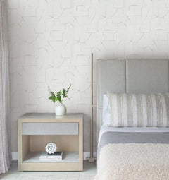 Minimalist bedroom featuring a light wood nightstand, white vase with greenery, decorative object, and a bed with gray and beige bedding set against Lyle Abstract Geometric Wallpaper by York Wallcoverings.