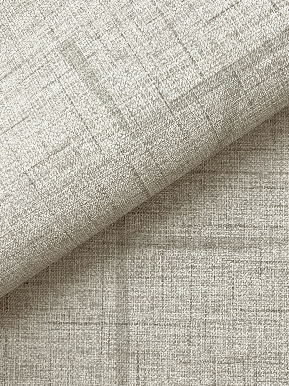 Close-up of York Wallcoverings’ Lyle Abstract Geometric Wallpaper in a light beige shade, showcasing its subtle woven texture and faint intersecting lines, with the wallpaper folded diagonally to reveal both the patterned surface and the underside.