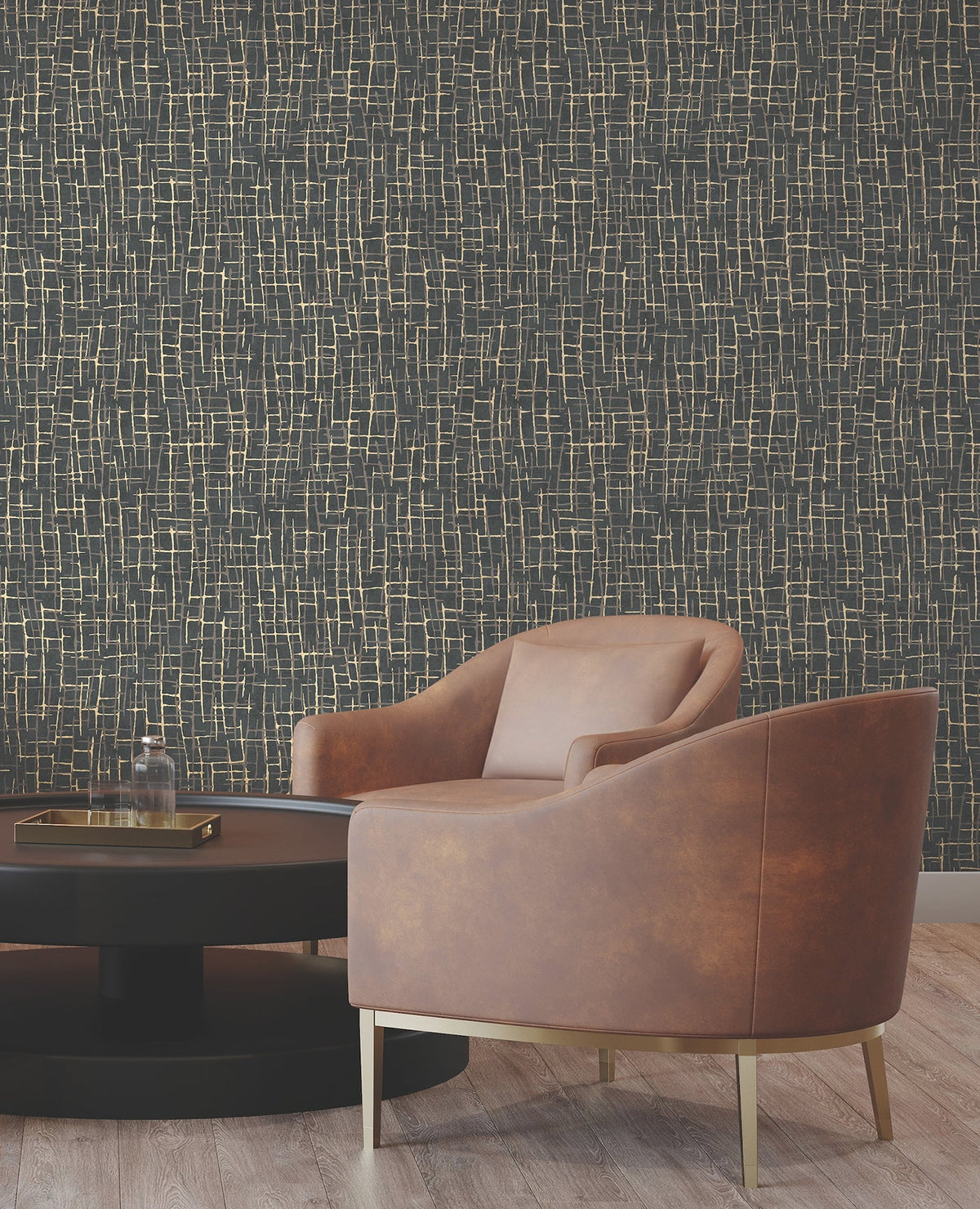 A modern brown leather chair with gold legs sits beside a round black coffee table. The background features York Wallcoverings’ Rian Linear Abstract Wallpaper in a dark hue with an abstract gold line pattern. The floor is light wood.