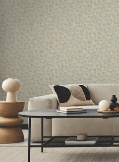 A modern living room featuring a light beige sofa, black and beige pillow, round wooden side table with a lamp, black coffee table, small decor items, and Ophidia Wallpaper by York Wallcoverings in neutral tones.