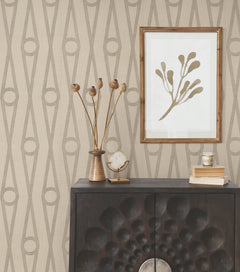 A modern console with textured doors displays decor items, while a framed botanical print hangs above. The walls are covered in York Wallcoverings’ Henlein Wallpaper, featuring a beige background with a repeating geometric pattern of ovals and lines.