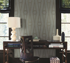 A desk with books, a white lamp, two vases, and a wooden chair in front of two windows. The wall features Henlein Wallpaper by York Wallcoverings in a geometric pattern with neutral tones.