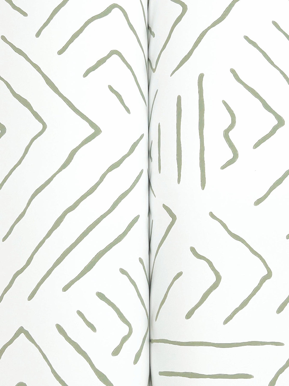 Sirih Wallpaper by York Wallcoverings features an abstract pattern of irregular, hand-drawn gray lines forming zigzags and triangular shapes on a white background; the image displays a central crease, indicating it is photographed from an open book or magazine.