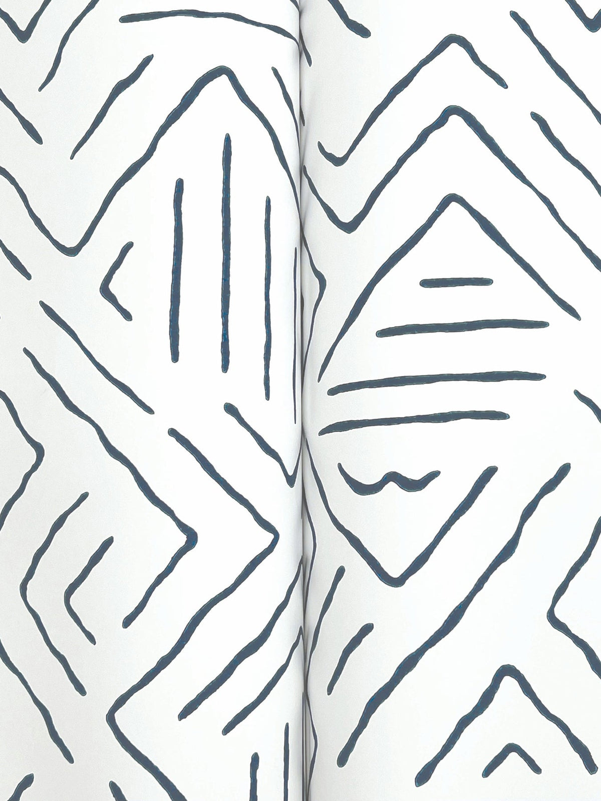 Close-up of Sirih Wallpaper by York Wallcoverings, featuring a white surface with abstract, hand-drawn dark blue zigzags and diamond shapes. Two vertical edges converge at the center, creating a subtle crease.