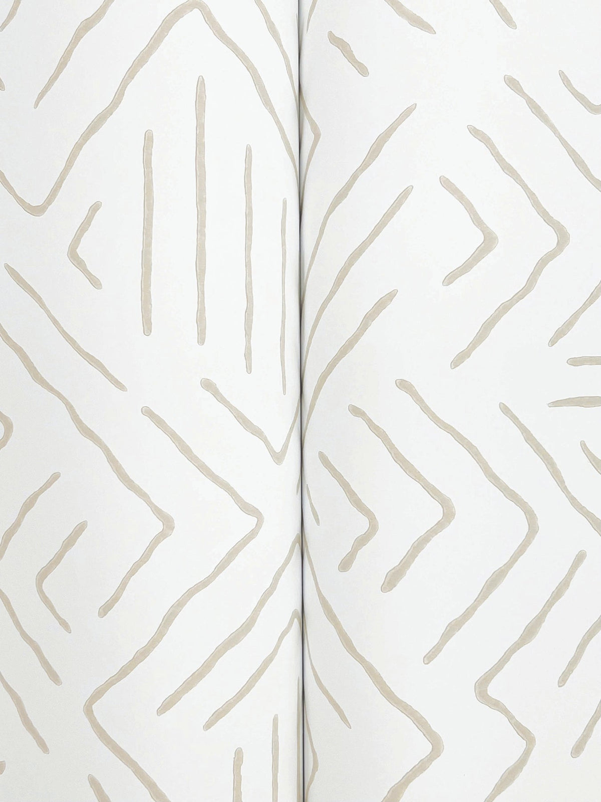 A close-up of the Sirih Wallpaper by York Wallcoverings showcases its white background adorned with a beige, hand-drawn zigzag and line pattern, creating a subtle geometric design. The wallpaper is pictured slightly folded down the center.