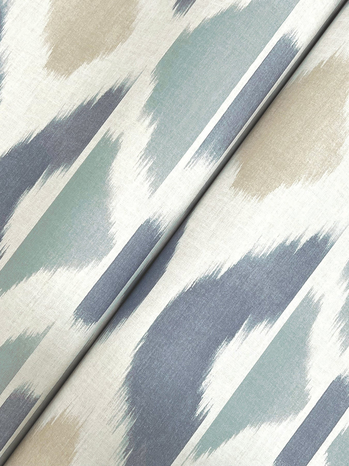 Experience the Patan Wallpaper by York Wallcoverings, featuring an abstract pattern of diagonal brushstrokes in blue, light green, beige, and white tones that create a soft, modern look. The wallpaper is shown gently folded along a diagonal line for added visual interest.