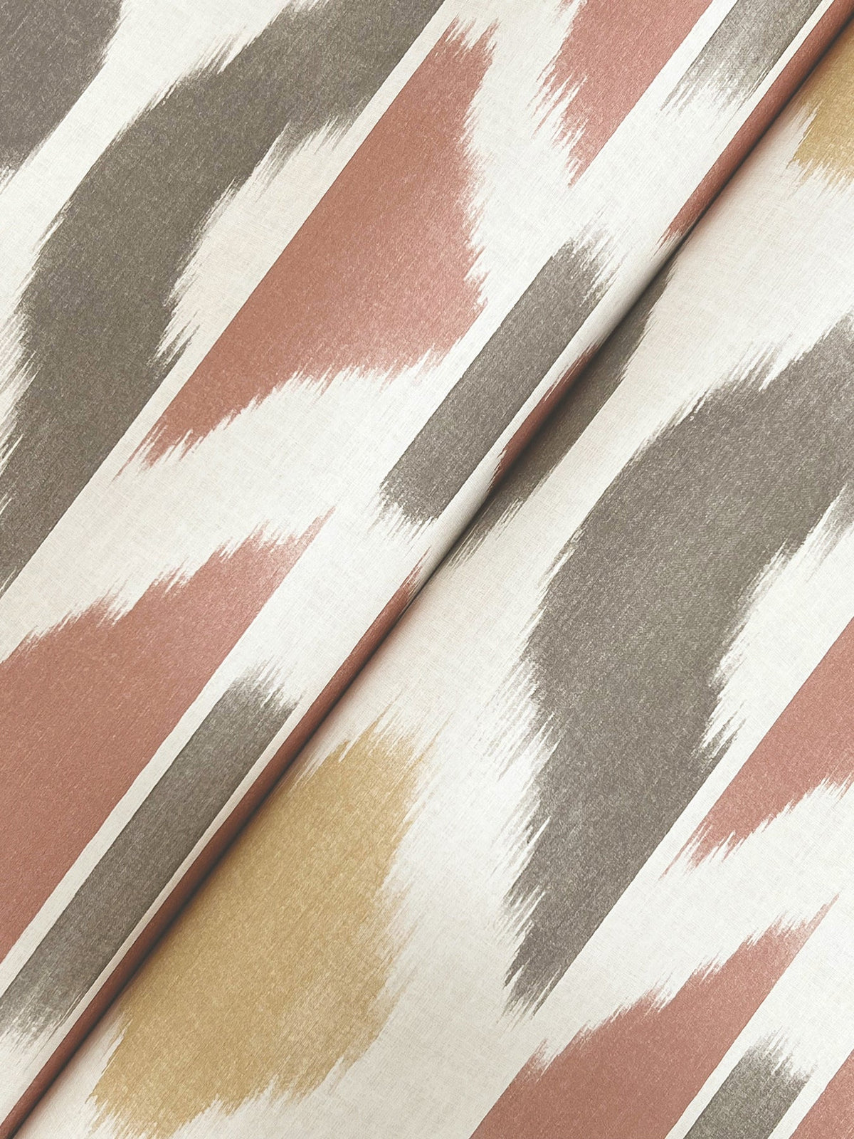 A close-up of the Patan Wallpaper by York Wallcoverings, featuring abstract, brushstroke-like patterns in muted pink, taupe, gold, and white tones, shown folded at an angle.
