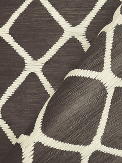 A close-up of York Wallcoverings’ Tonga Wallpaper, showcasing its dark woven texture with a white geometric diamond pattern, with one corner lifted to highlight the design and material.