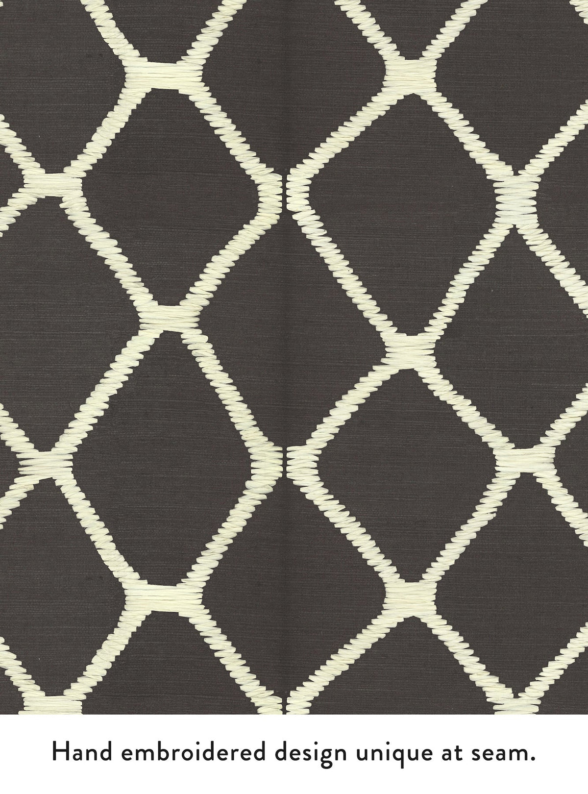 Tonga Wallpaper by York Wallcoverings features a dark background with a cream, diamond-shaped hand-embroidered pattern. A central seam introduces a subtle design variation, making the embroidery at the join distinctly unique.