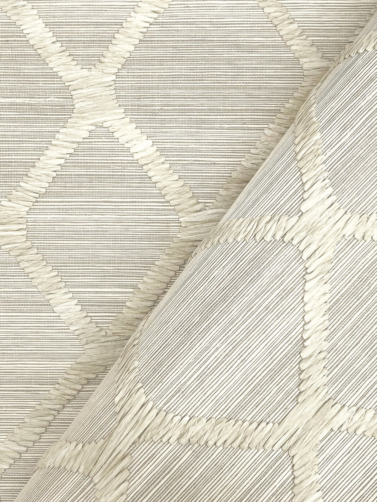 A close-up of Tonga Wallpaper by York Wallcoverings in light beige, featuring a raised geometric diamond pattern, with one section slightly folded over to highlight the textured design from both flat and angled perspectives.