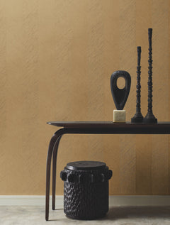 A modern interior showcases a dark table with two tall candlesticks, an abstract black sculpture, and a textured basket underneath, all set against York Wallcoverings’ Chevron Wallpaper.