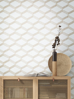 A wooden cabinet with books and decor sits against a wall adorned in York Wallcoverings’ Palisades Paperweave Wallpaper. On top are an open book, a tall vase with dried branches, and a round, textured decorative plate.