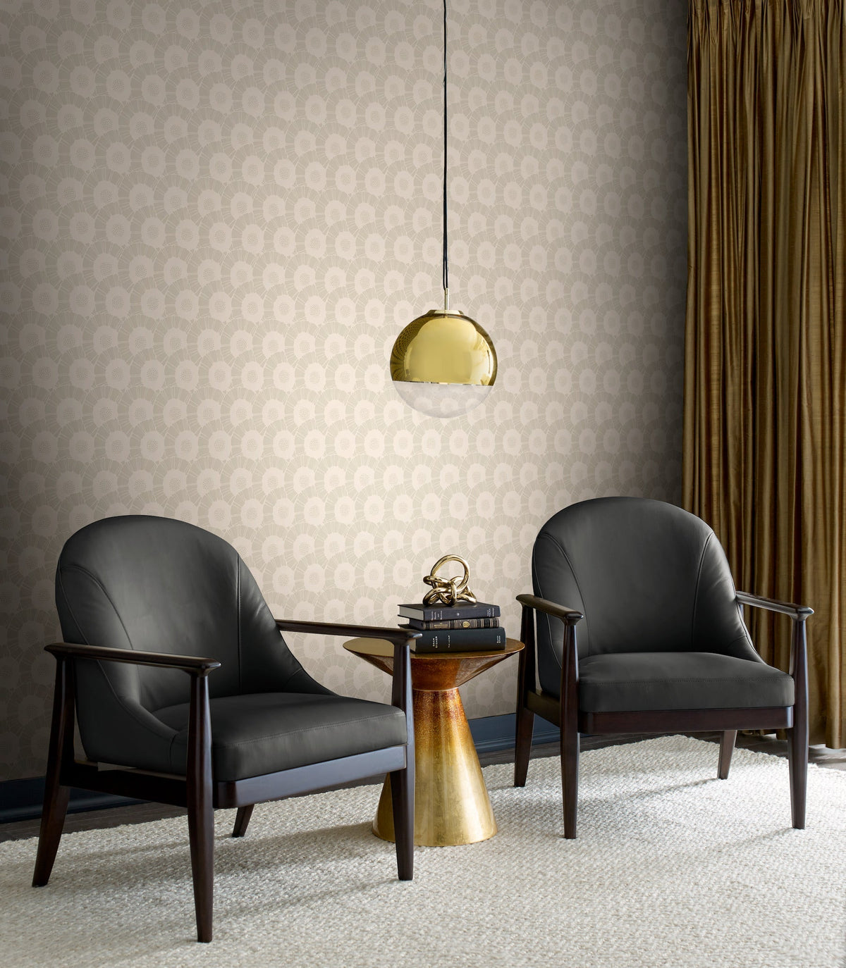 Two black armchairs face a small gold side table with books and a decorative object. A gold pendant lamp hangs above, and gold curtains frame the patterned Coco Bloom Wallpaper by York Wallcoverings in beige.