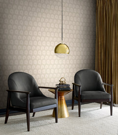 Two black armchairs face a small gold side table with books and a decorative object. A gold pendant lamp hangs above, and gold curtains frame the patterned Coco Bloom Wallpaper by York Wallcoverings in beige.