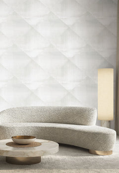 In Clay Wallpaper by York Wallcoverings in a light gray repeating diamond pattern on a wall behind a curved sofa, a marble coffee table, and a tall floor lamp.