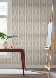 A wooden desk with art supplies and a plant sits by a window; an easel stands nearby against Escalante Wallpaper by York Wallcoverings in a bright room.
