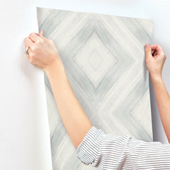 Hands holding a strip of grey and white geometric diamond Ballad Wallpaper against a wall.