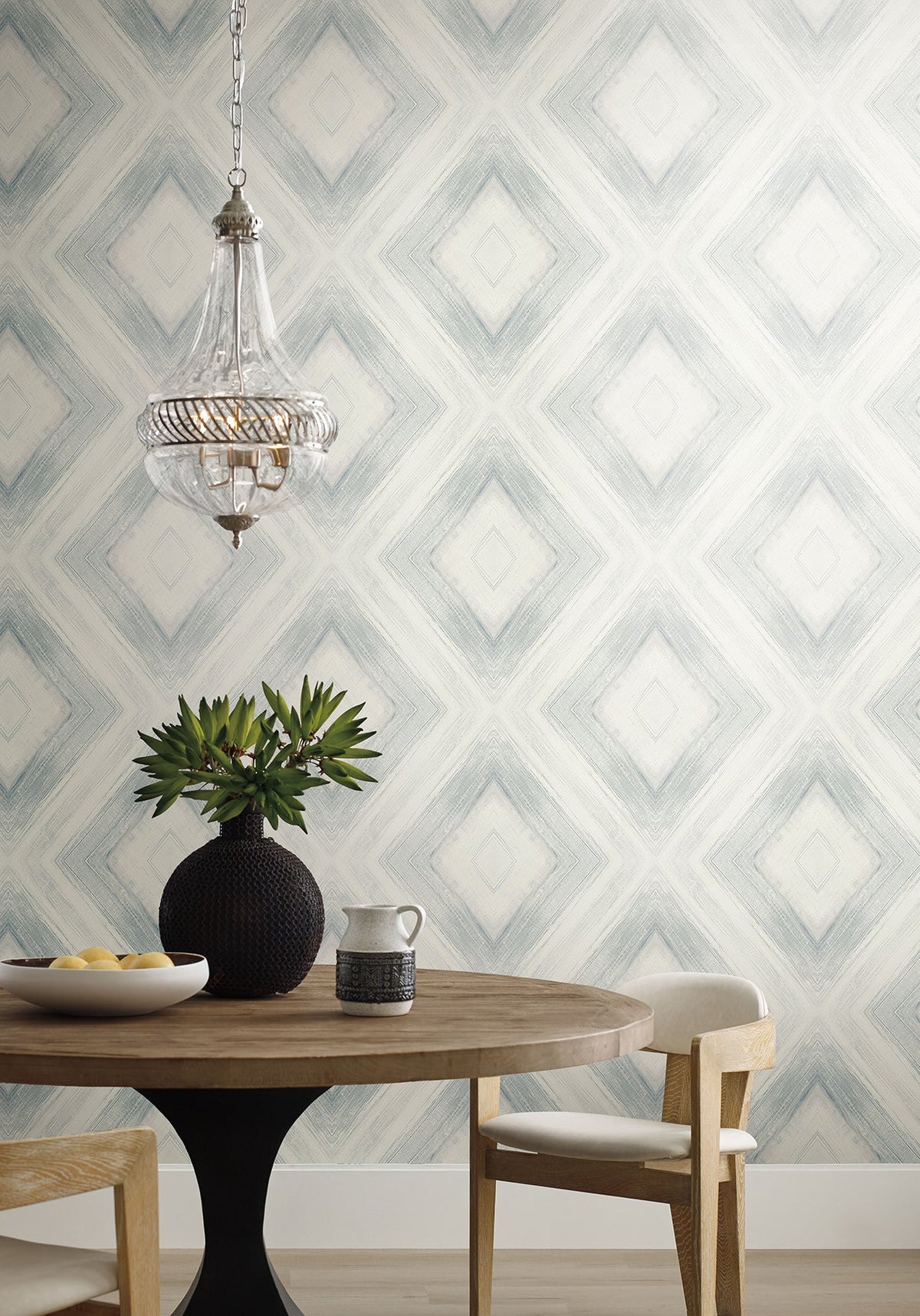 Ballad Wallpaper featuring a blue and white geometric diamond pattern behind a round wooden dining table and a glass pendant light.