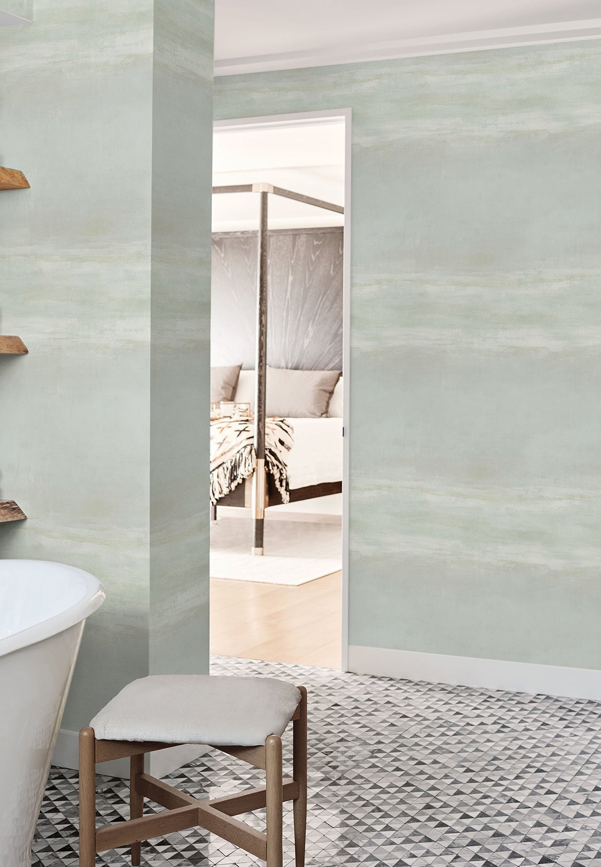 Serene Reflection Wallpaper in light green with a subtle, horizontal brushstroke texture installed on walls in a bathroom and bedroom doorway.