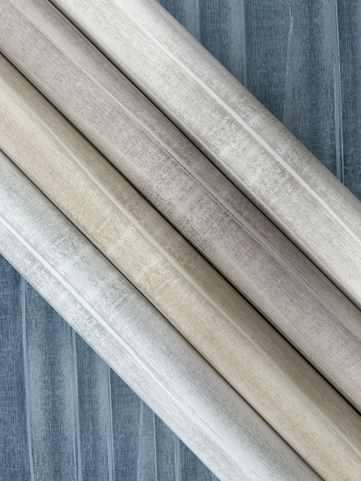 Four rolls of York Wallcoverings Grey Stone Wallpaper displayed diagonally, showing shades of grey, taupe, and cream with a textured, stone-like appearance.