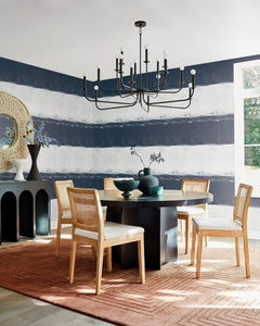 A dining room with a round black table and four cane-back chairs, featuring walls covered in York Wallcoverings Ink Wash Wallpaper with a dark navy and white horizontal design.