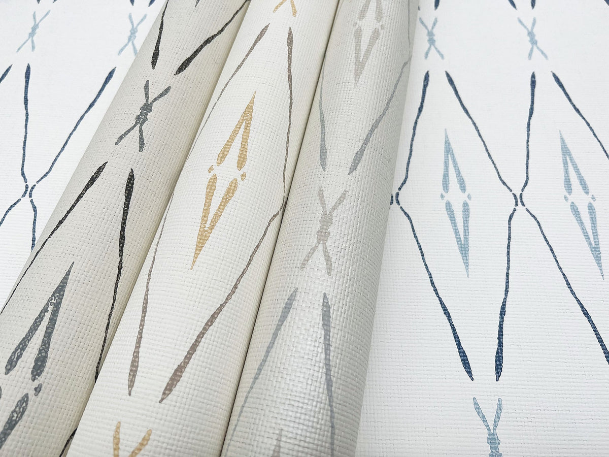 Three rolls of York Wallcoverings Artifact Silhouettes Wallpaper stand upright next to a flat sample, all featuring a repeating diamond-shaped ikat pattern in shades of blue, grey, and tan on a white textured background.