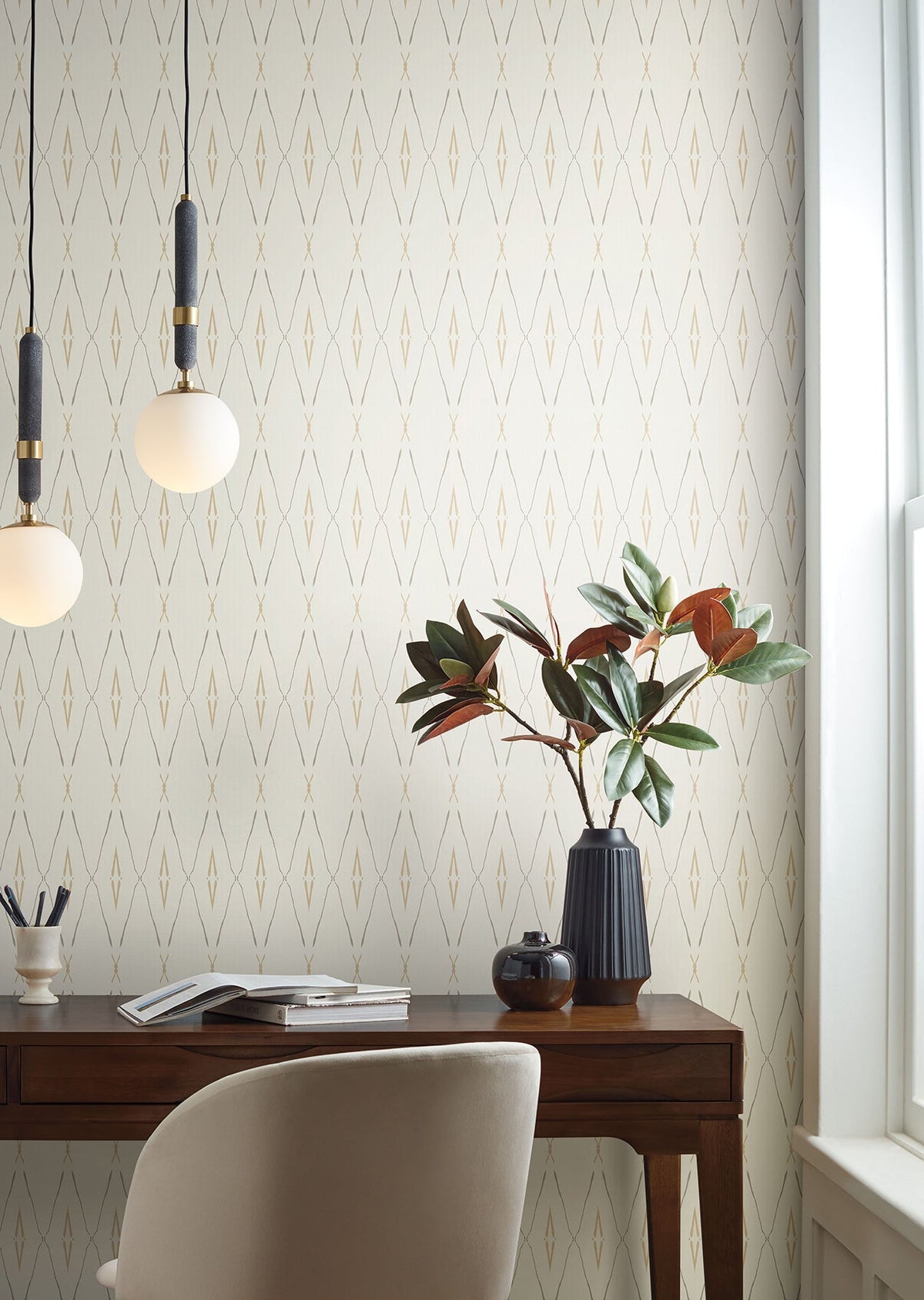 Artifact Silhouettes Wallpaper featuring a repeating pattern of thin, tan diamond shapes on a cream background, installed behind a wooden desk with a plant and pendant lights.