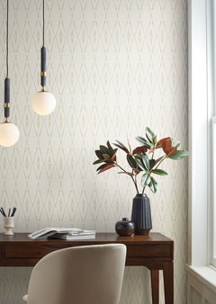 Artifact Silhouettes Wallpaper featuring a repeating pattern of thin, tan diamond shapes on a cream background, installed behind a wooden desk with a plant and pendant lights.