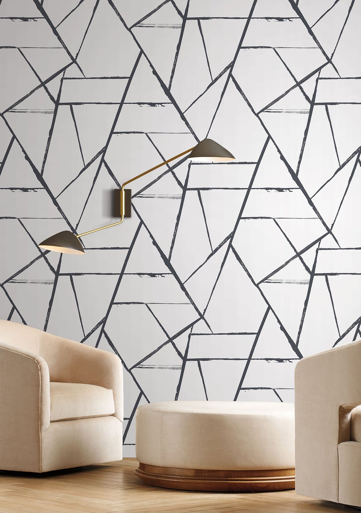 York Wallcoverings Intersect wallpaper features a black-and-white geometric pattern of overlapping, textured lines on a wall behind two armchairs and an ottoman with a wall-mounted double-arm light.