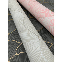 Two rolls of Candice Olson Luminous Gingko Wallpaper featuring a gray, pink, and white ginkgo leaf pattern rest on top of a dark gray sheet of the same wallpaper with gold veining.
