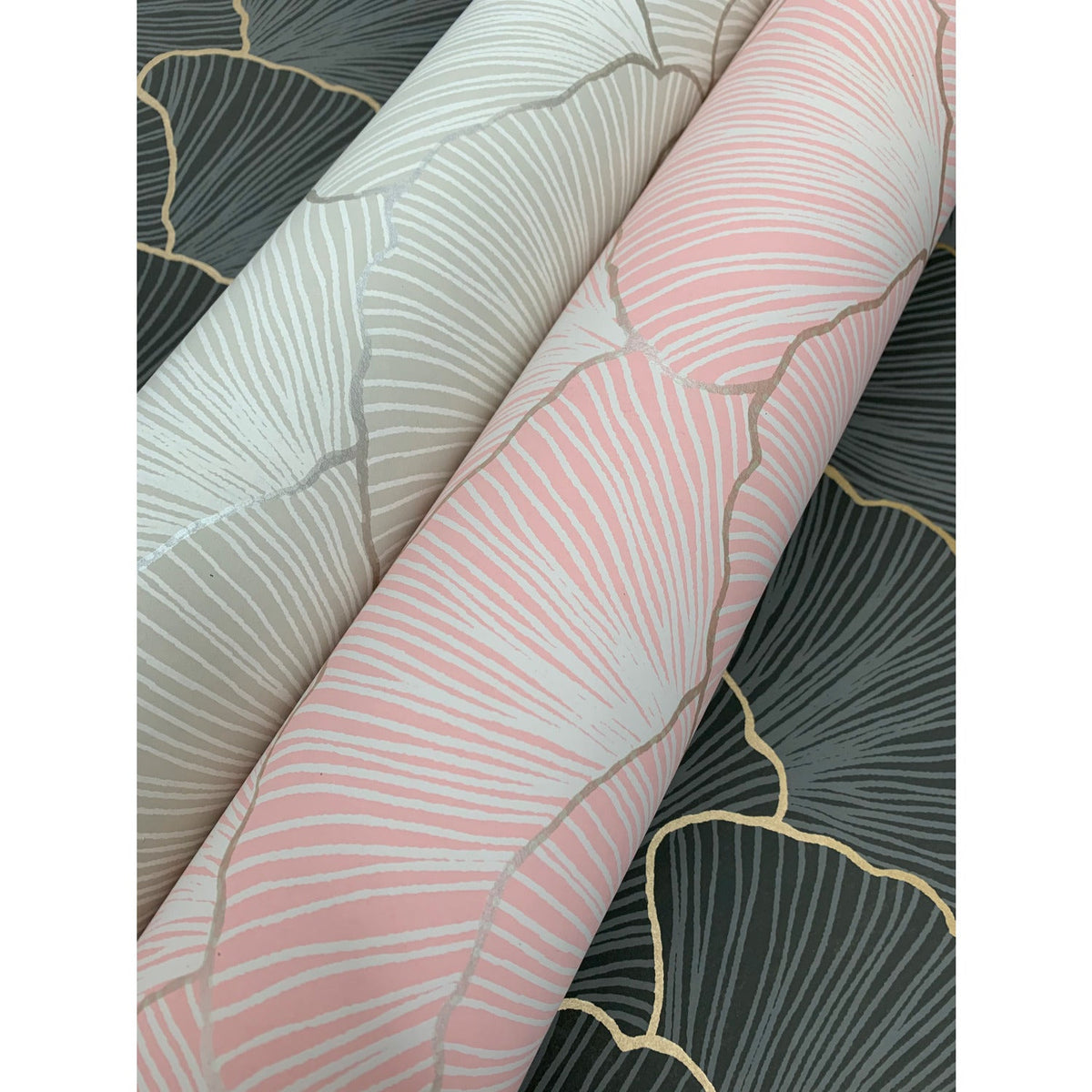 Two rolls of Candice Olson Luminous Gingko Wallpaper in pink and cream, laid over sections of the same pattern in dark gray.