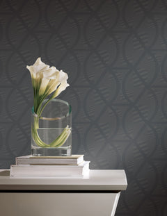A glass vase of white calla lilies sits on two books atop a side table against Candice Olson Opposites Attract Wallpaper by York Wallcoverings, featuring a dark, geometric dotted pattern.