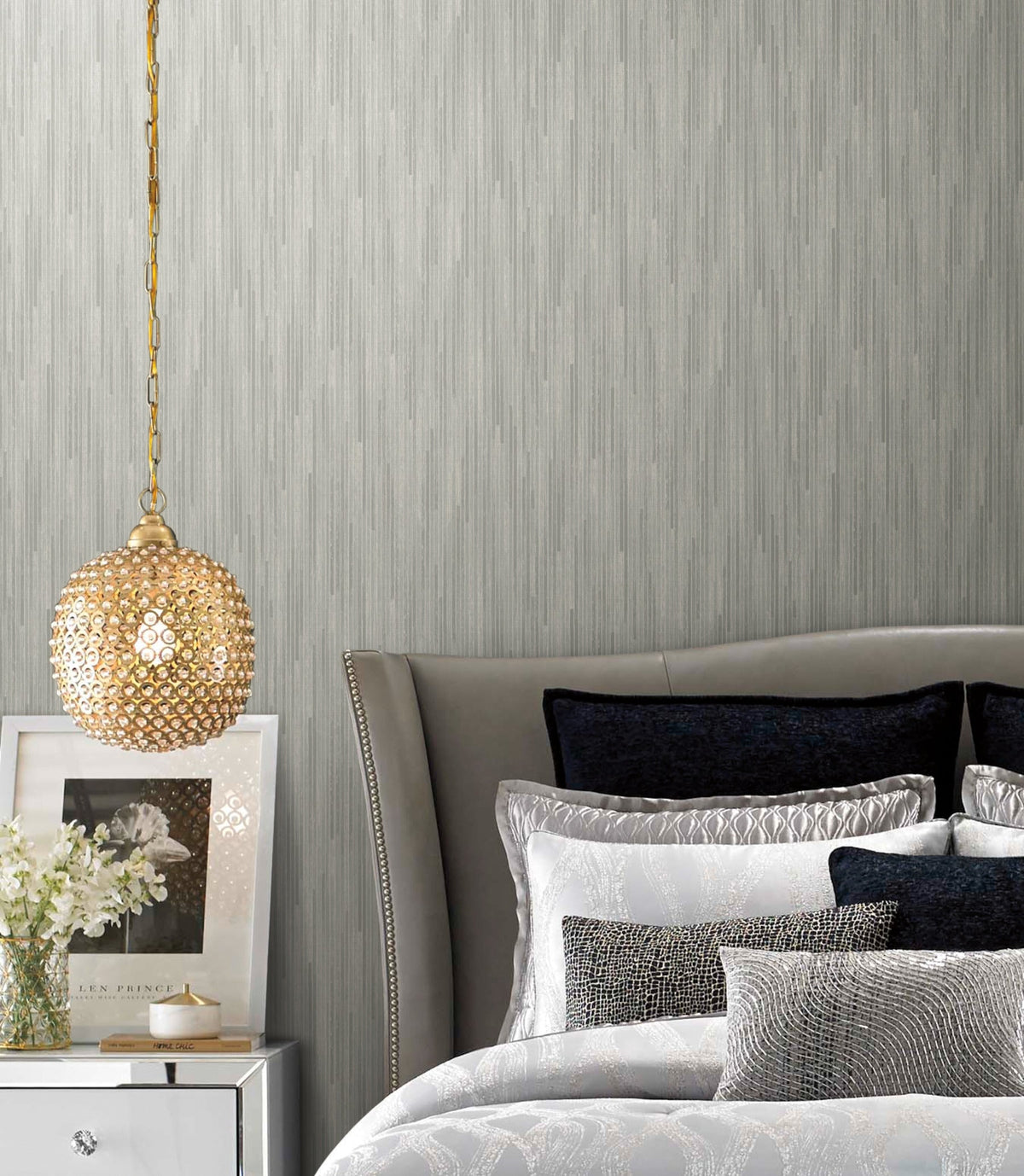 A bedroom featuring grey Candice Olson Bargello Wallpaper with vertical-striped texture, a crystal pendant light, and a bed with layered pillows.