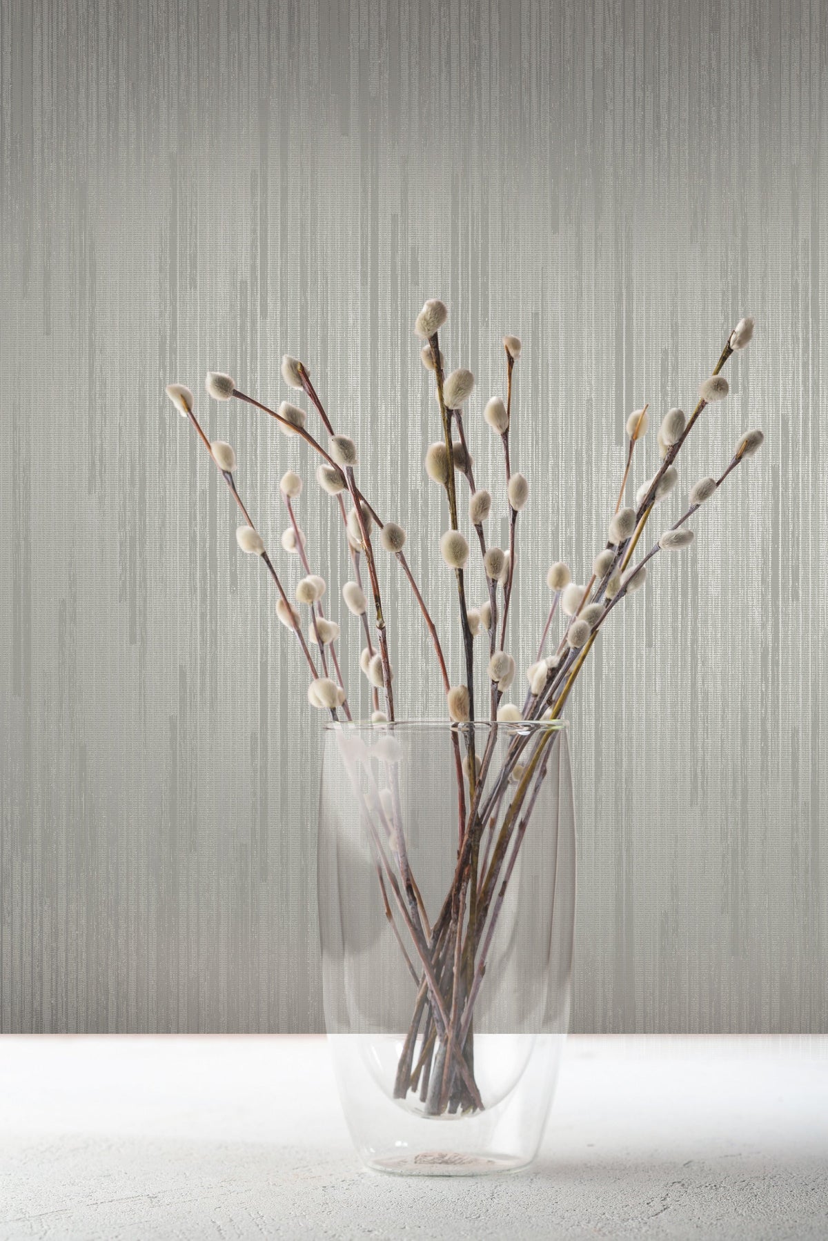 A glass vase filled with pussy willow branches stands against grey Candice Olson Bargello Wallpaper by York Wallcoverings.