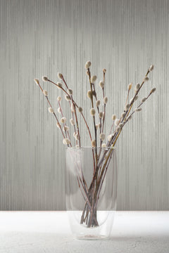 A glass vase filled with pussy willow branches stands against grey Candice Olson Bargello Wallpaper by York Wallcoverings.