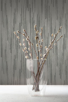 A clear glass vase holding pussy willow branches in front of gray Candice Olson Bargello Wallpaper with a vertical textured pattern.