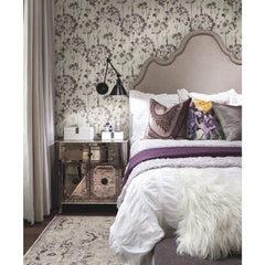 A bedroom features Candice Olson Flourish Wallpaper with a purple and grey botanical print behind an upholstered headboard and a mirrored nightstand.