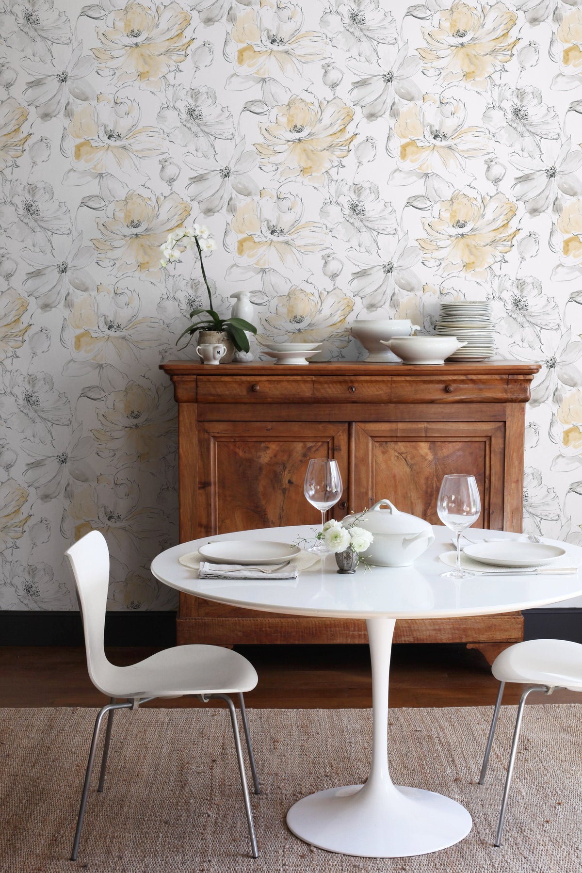 Floral Dreams Wallpaper featuring a watercolor-style pattern of large, pale yellow and grey flowers against a white background, shown in a dining area.