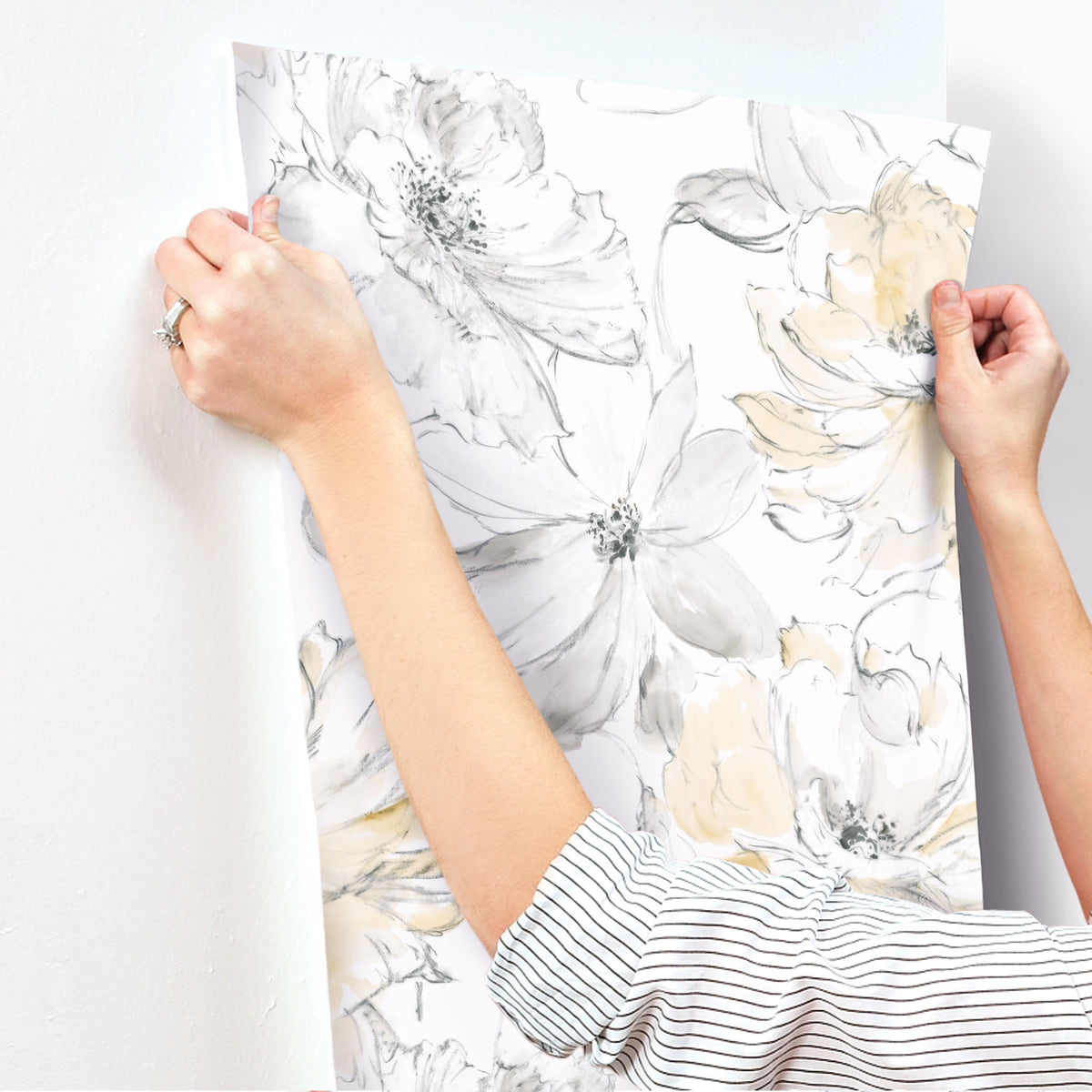 Hands applying Floral Dreams Wallpaper featuring watercolor-style gray and yellow flowers to a white wall.