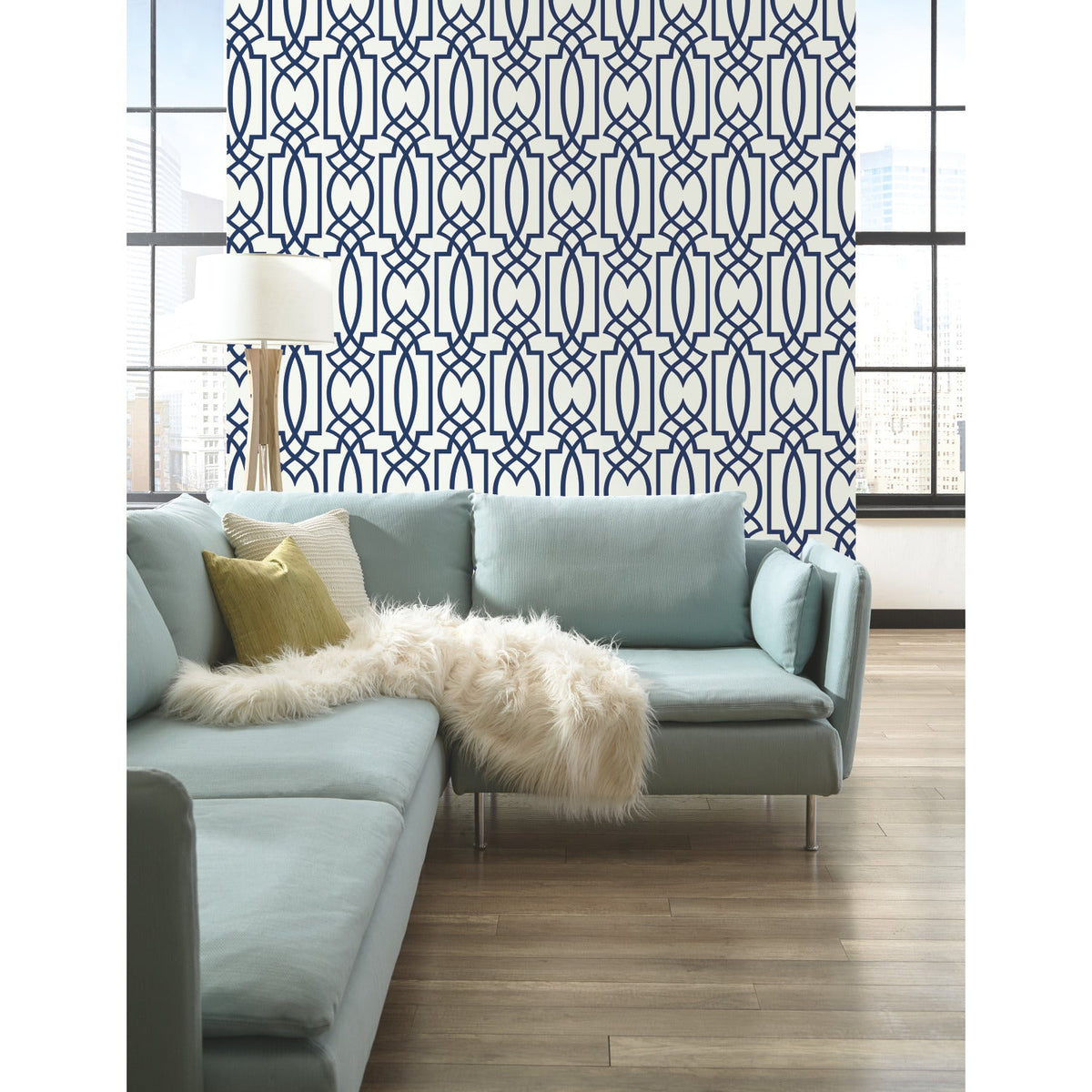 Large Lattice Wallpaper by York Wallcoverings with a blue geometric lattice pattern of interlocking ovals and rectangles, installed on a wall behind a light blue sectional sofa.